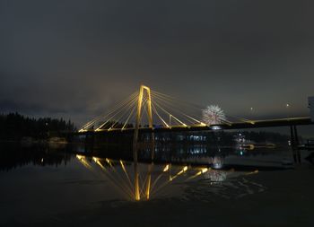 Illuminated bridge over river against sky at night