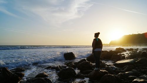 Rear view of teenage girl standing at beach during sunset