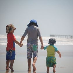 Rear view of friends on sea shore against sky