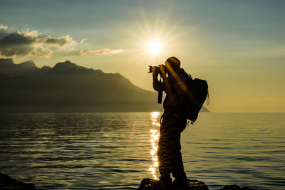 Silhouette man photographing sea against sunset sky