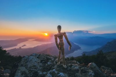 Rear view of man standing on rock against sky during sunset