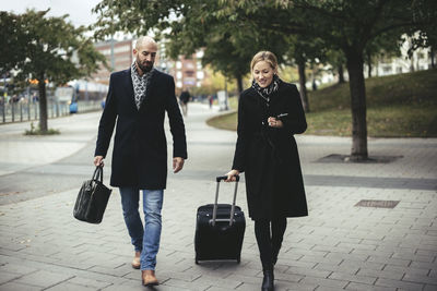 Full length of business people with luggage walking on sidewalk