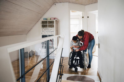 Mother fastening wheelchair buckle for disabled son at home