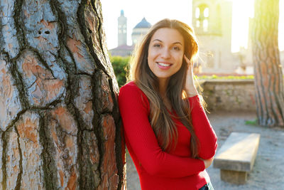 Portrait of smiling young woman standing by tree trunk