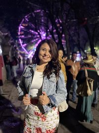 Portrait of young woman standing against illuminated city at night
