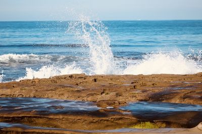 Waves splashing on rocks at shore against sky