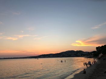 Silhouette people at beach against sky during sunset