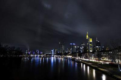 Illuminated buildings by river against sky at night