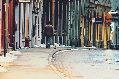 Rear view of man walking on street in city during winter