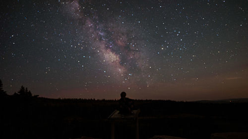 Silhouette man sitting against star field at night