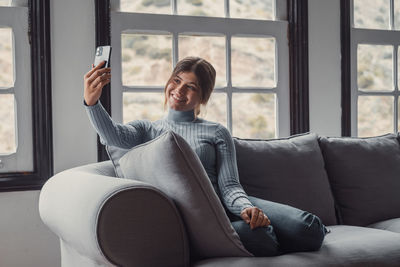 Young woman using phone while sitting on sofa at home