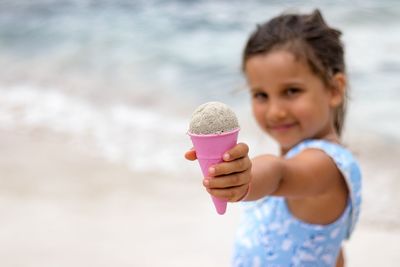 Portrait of girl holding sand in cone while standing at beach