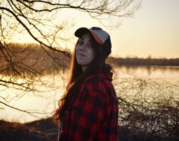 Young woman standing by lake against sky during sunset