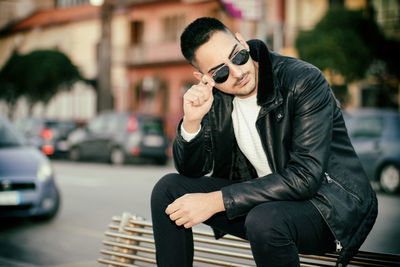 Young man wearing sunglasses sitting in city