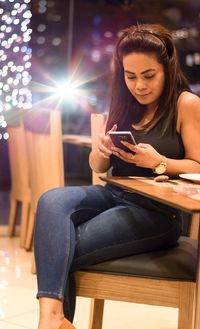 Young woman using phone while sitting on chair at restaurant