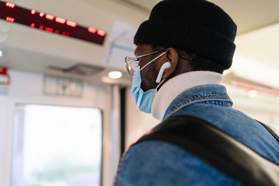 Back view of african american male passenger in mask standing at doors while traveling during coronavirus epidemic