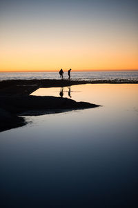 Silhouette people on beach against sky during sunset