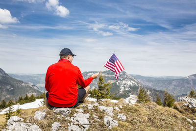 Man sitting on rock by mountain against sky