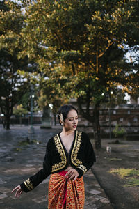 Young woman wearing traditional clothing standing on footpath against trees in park
