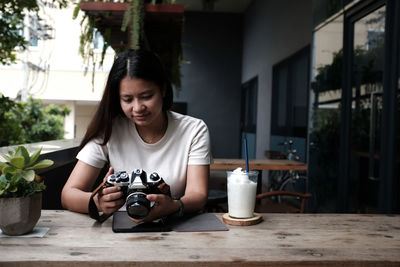 Young woman photographing while sitting on table