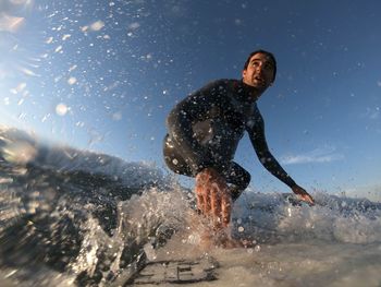 Low angle view of man surfing on sea against blue sky