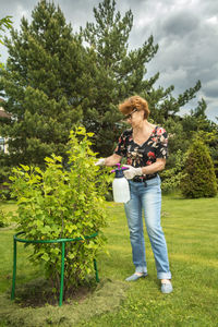 Full length of senior woman holding umbrella standing against trees