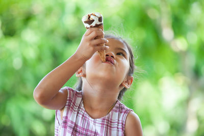 Close-up of cute girl eating ice cream cone while sitting against trees at park