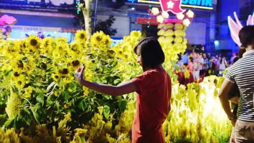 Teenage girl taking selfie by sunflower plants in city