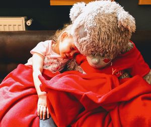 Rear view of a child resting with the huge teddy bear covered with a blanket