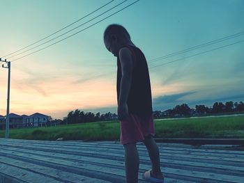 Boy standing on land against sky during sunset