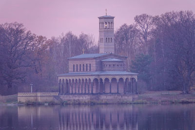 Built structure by lake against sky at dusk