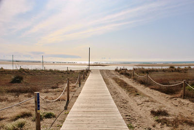 Boardwalk leading towards sea against sky