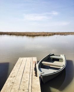 Boat moored by jetty in lake against sky