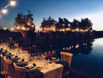 Illuminated table by trees against sky at night