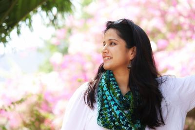 Thoughtful young woman smiling while standing against flowers