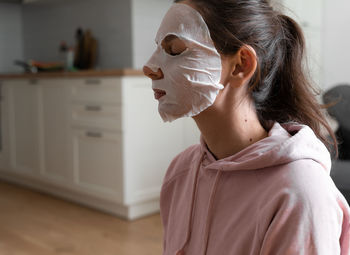 Side view of young woman wearing mask sitting at home