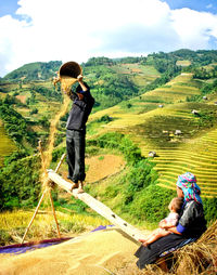 Rear view of couple sitting on mountain against sky