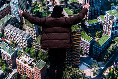 Rear view of man standing with arms raised over buildings