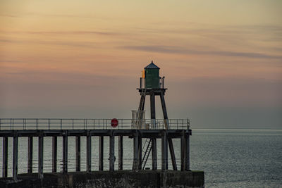 Lighthouse by sea against sky during sunset