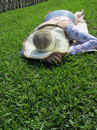 Woman wearing hat lying on grassy field at yard