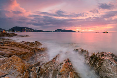 Silhouette man fishing on rock at dusk with twilight sky in kalim beach at patong, phuket, thailand