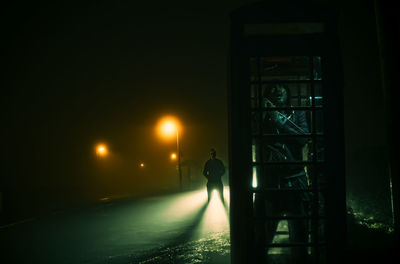 Man talking in telephone booth at night