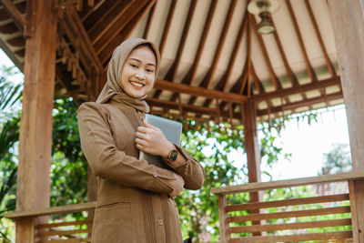 Portrait of young woman standing against trees