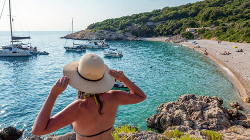 Rear view of young woman with sun hat looking at beautiful beach in summer. boats, sea, vacation.