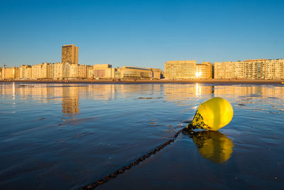 Bright yellow buoy on the beach of ostend with city skyline in the background