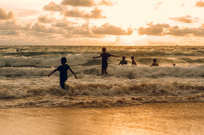 People enjoying on beach against sky during sunset