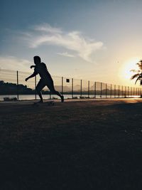 Low angle view of man skateboarding on road by river during sunset