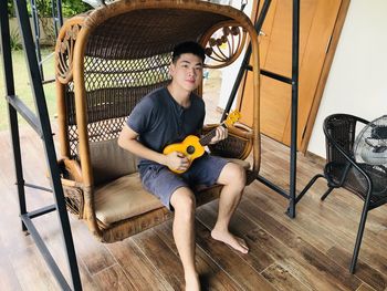 Portrait of young man sitting on chair and playing ukulele 