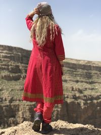 Rear view of woman standing on rock against sky