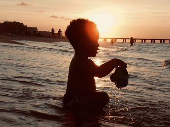 Silhouette boy on beach against sky during sunset